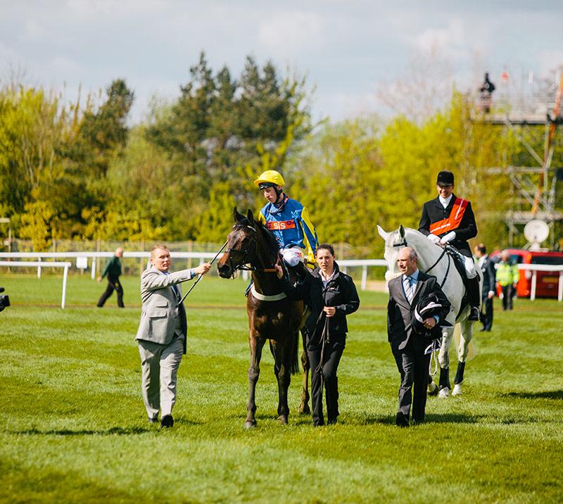 Horse being led by it's owner, trainer and jockey.