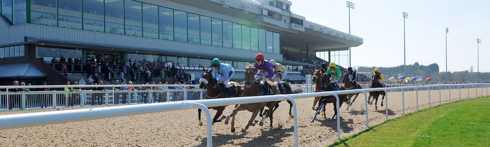 Group of jockeys racing past crowds watching from the grandstand at Wolverhampton Racecourse.